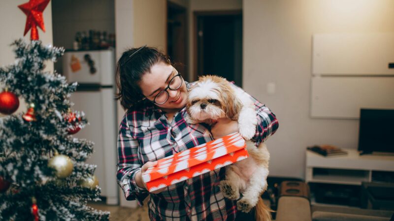 a woman holding a dog in front of a christmas tree